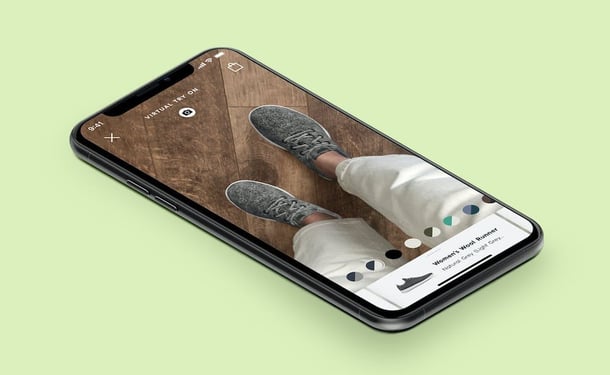 A cellphone shows a customer using AR to try on a pair of AllBirds
