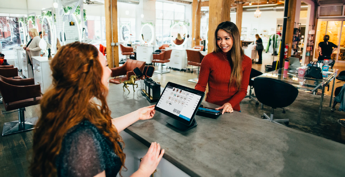 A retailer and a customer using an in-store POS system while smiling and chatting.