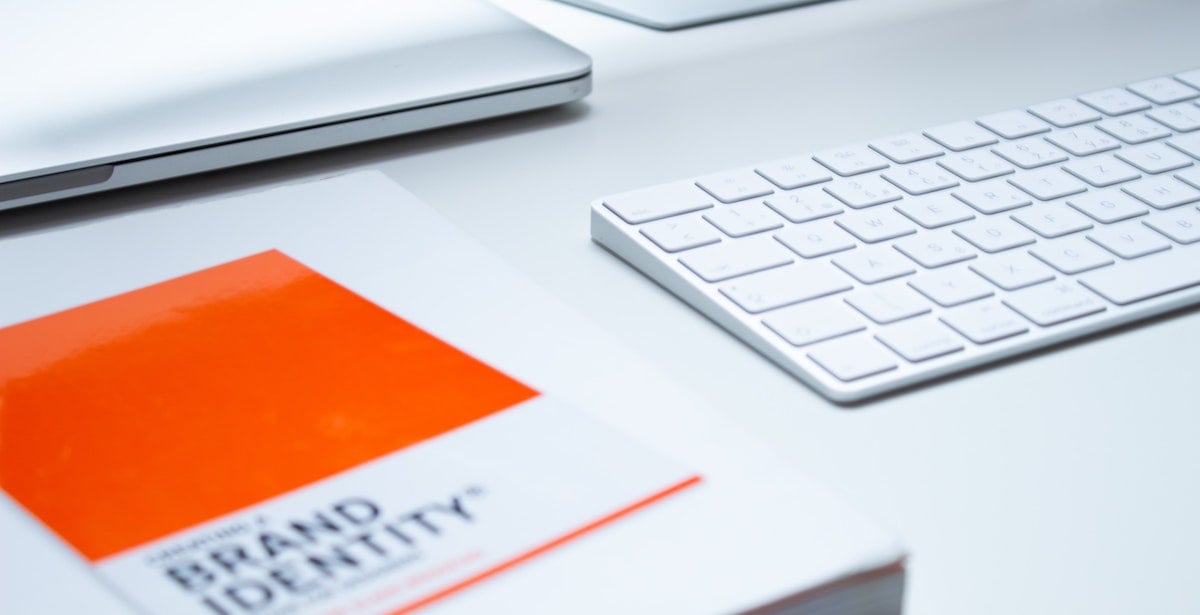 A book titled 'Brand Identity' sits on a desk next to a keyboard