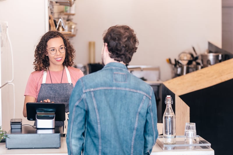 A women serves a man from behind a shop counter.