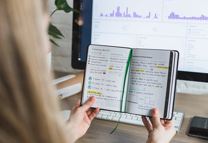 A woman checks a marketing notebook against her computer screen